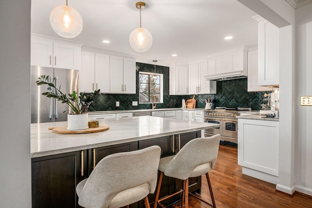 kitchen featuring a breakfast bar, white cabinetry, stainless steel appliances, dark hardwood / wood-style floors, and decorative light fixtures