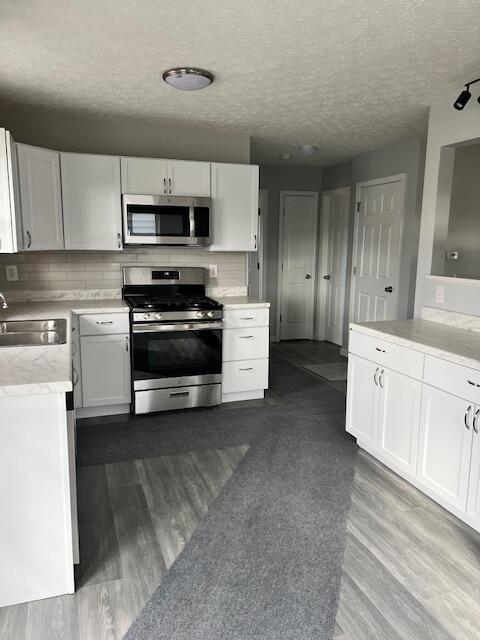 kitchen with sink, white cabinets, a textured ceiling, and appliances with stainless steel finishes