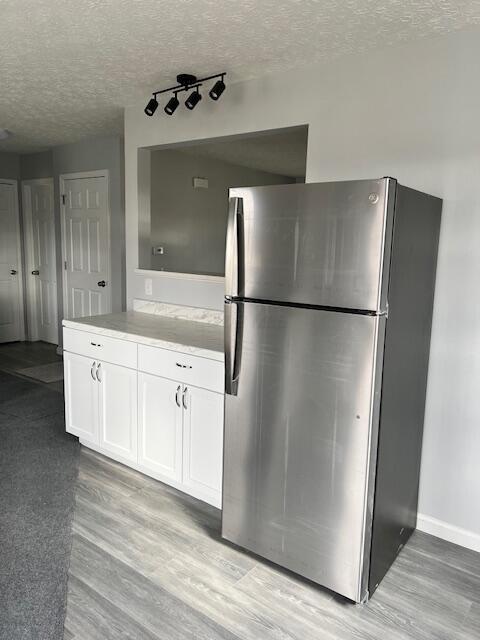 kitchen with white cabinets, light hardwood / wood-style floors, a textured ceiling, and stainless steel refrigerator