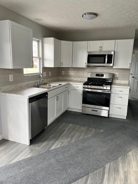 kitchen with sink, stainless steel appliances, white cabinetry, and dark wood-type flooring