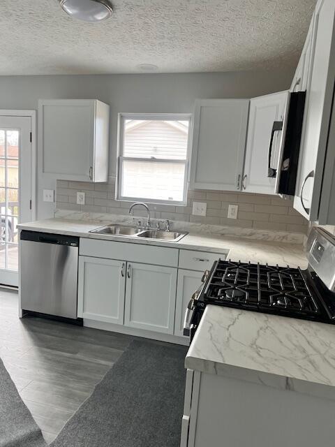 kitchen with white cabinets, stainless steel appliances, light stone countertops, decorative backsplash, and sink