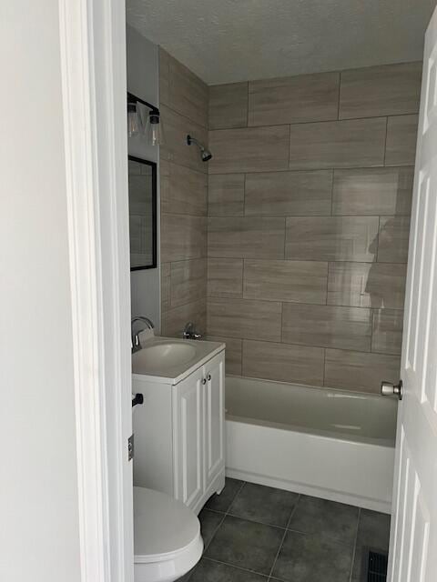 full bathroom with tile patterned flooring, tiled shower / bath combo, vanity, and toilet