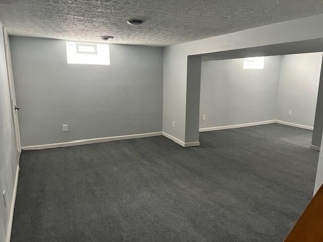 basement featuring a textured ceiling and dark colored carpet