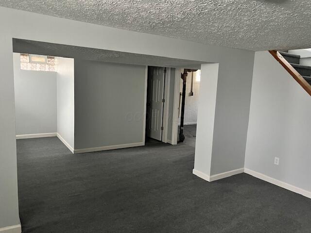 basement featuring a textured ceiling and dark colored carpet