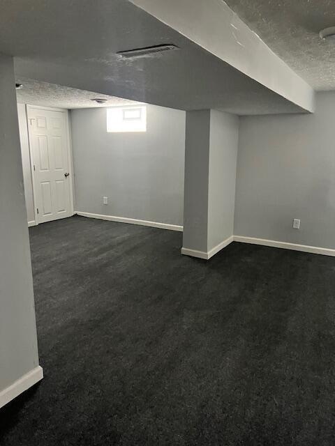 basement with a textured ceiling and dark carpet