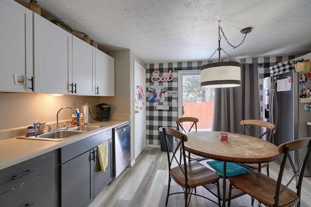 kitchen featuring light wood-type flooring, a sink, a textured ceiling, appliances with stainless steel finishes, and light countertops