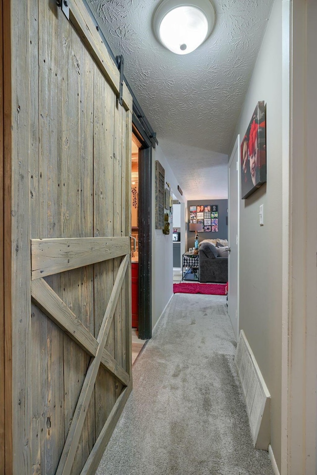 hallway with wooden walls, carpet, visible vents, a textured ceiling, and a barn door