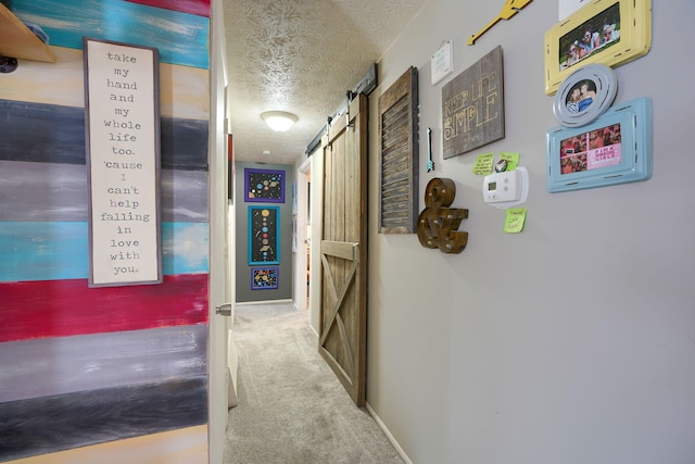 hallway with a barn door, baseboards, a textured ceiling, and carpet