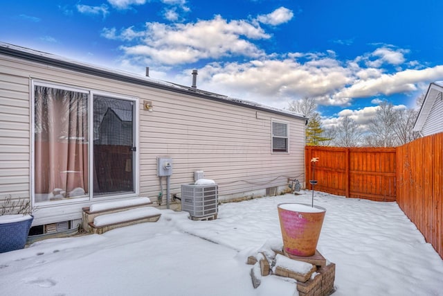 snow covered patio featuring central AC and fence