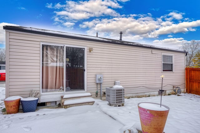 snow covered house featuring cooling unit and fence