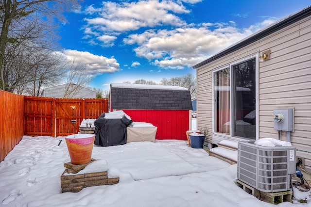 snow covered patio with a storage unit, cooling unit, an outdoor structure, and a fenced backyard