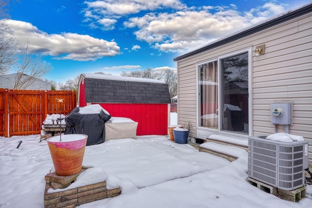 snow covered patio featuring an outbuilding, a shed, fence, a grill, and central AC unit