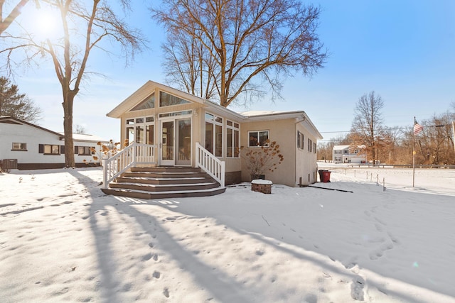 snow covered rear of property with a sunroom