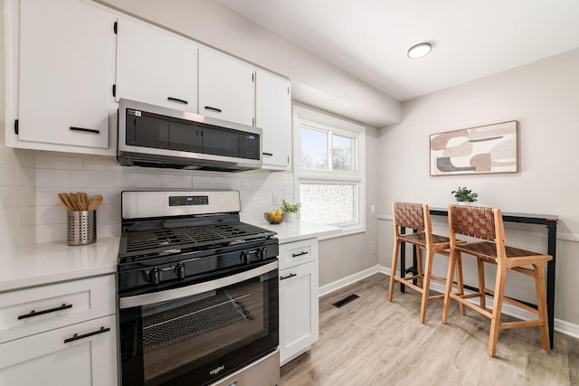 kitchen featuring white cabinets, stainless steel appliances, light hardwood / wood-style floors, and decorative backsplash