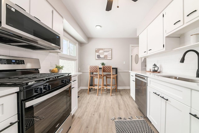 kitchen with stainless steel appliances, sink, white cabinets, light hardwood / wood-style floors, and backsplash