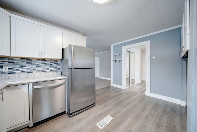 kitchen with tasteful backsplash, crown molding, light hardwood / wood-style flooring, appliances with stainless steel finishes, and white cabinets