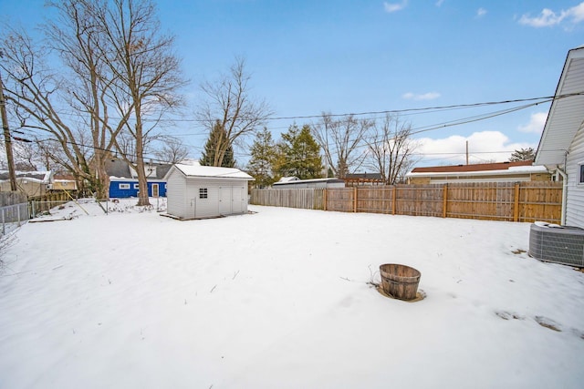 yard layered in snow featuring central AC unit, an outdoor fire pit, and a storage unit