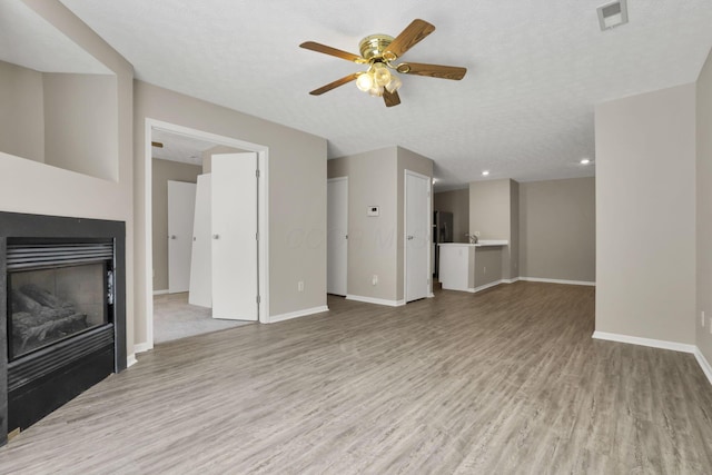 unfurnished living room with a textured ceiling, ceiling fan, and light hardwood / wood-style floors