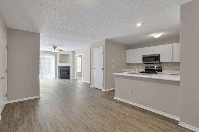 kitchen with white cabinetry, kitchen peninsula, stainless steel appliances, dark hardwood / wood-style floors, and a textured ceiling