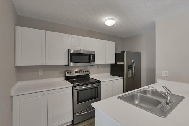 kitchen with stainless steel appliances, dark hardwood / wood-style flooring, a textured ceiling, white cabinets, and sink