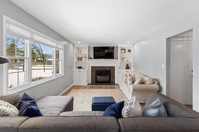 living room featuring built in shelves, a tiled fireplace, and light wood-type flooring