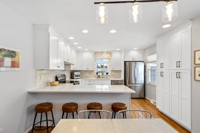 kitchen featuring appliances with stainless steel finishes, a kitchen bar, white cabinetry, sink, and hanging light fixtures