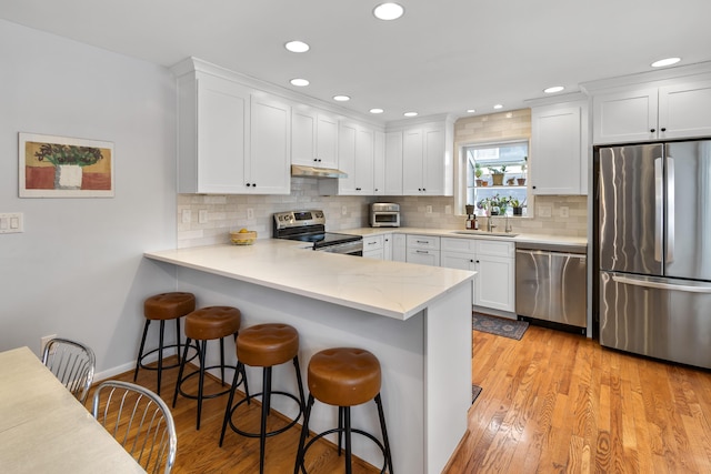 kitchen featuring light hardwood / wood-style floors, sink, appliances with stainless steel finishes, a breakfast bar area, and white cabinets