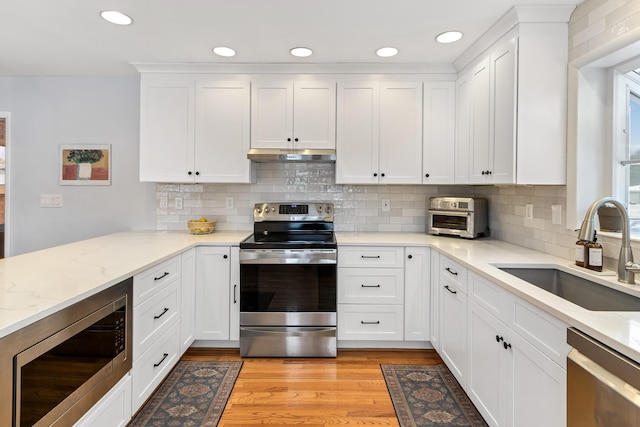 kitchen featuring white cabinetry, stainless steel appliances, backsplash, light stone counters, and sink