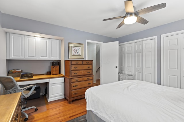 bedroom with ceiling fan, two closets, built in desk, and light wood-type flooring