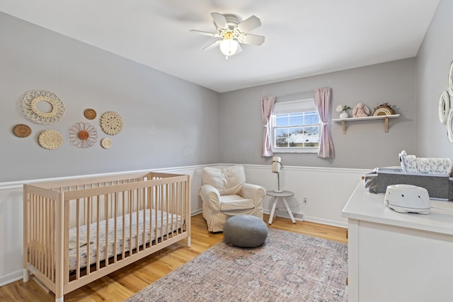 bedroom featuring ceiling fan, a crib, and light hardwood / wood-style flooring