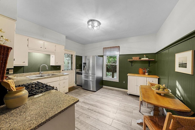 kitchen with stainless steel appliances, sink, white cabinets, light stone counters, and light hardwood / wood-style flooring