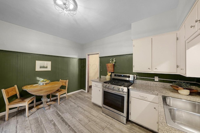 kitchen with sink, white cabinetry, stainless steel gas range, light hardwood / wood-style floors, and wood walls