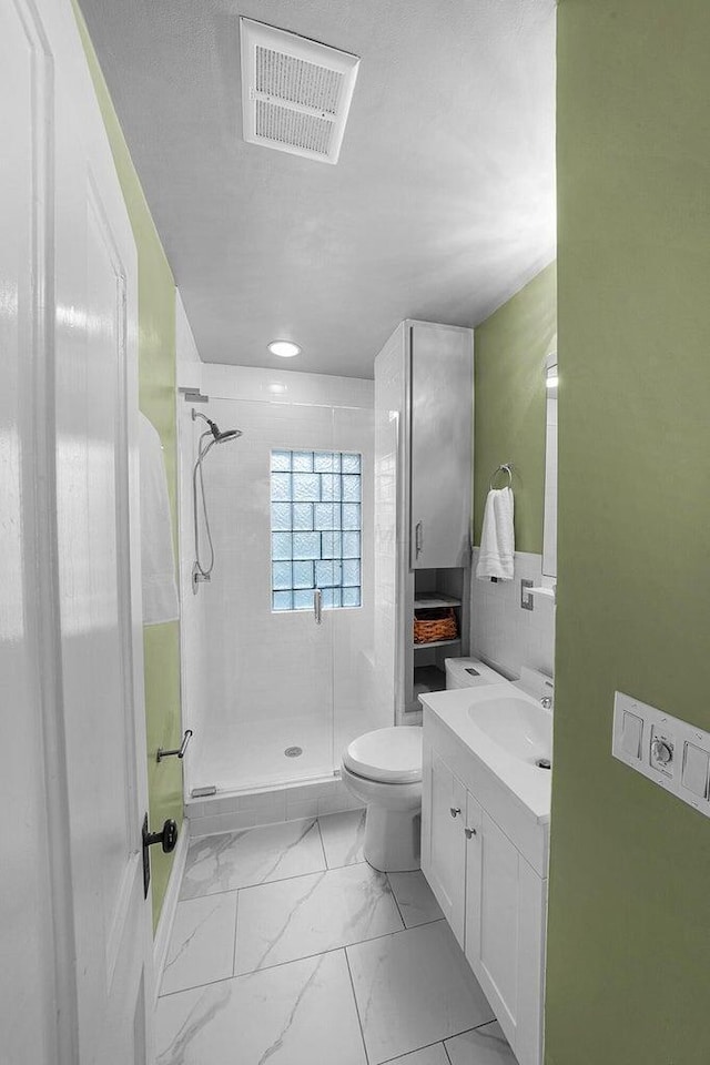 bathroom featuring toilet, a tile shower, vanity, and tile walls