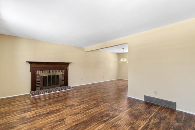 unfurnished living room with a brick fireplace, dark wood-type flooring, beamed ceiling, and an inviting chandelier