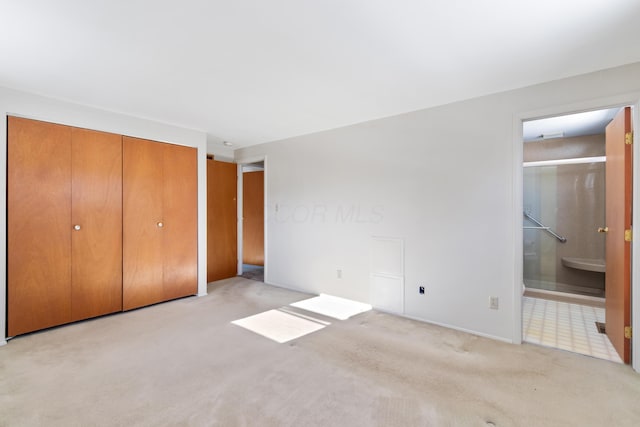 unfurnished bedroom with a closet, ensuite bathroom, and light colored carpet