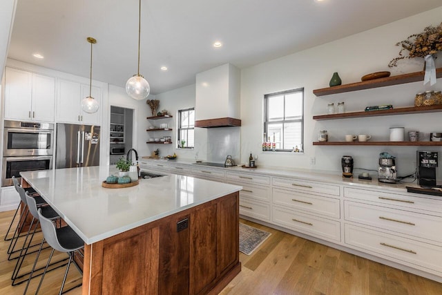 kitchen featuring sink, a kitchen island with sink, stainless steel appliances, decorative light fixtures, and custom exhaust hood