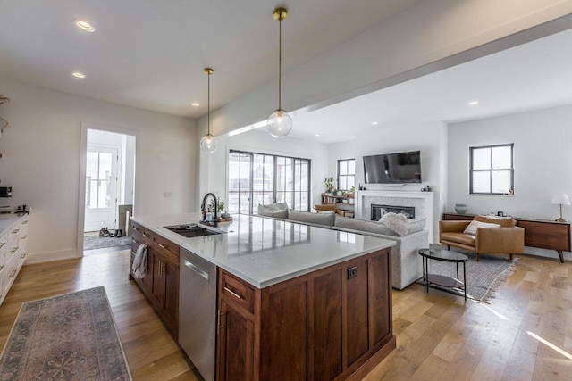 kitchen featuring pendant lighting, an island with sink, sink, stainless steel dishwasher, and light hardwood / wood-style flooring