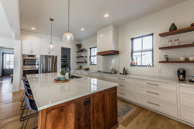 kitchen with premium range hood, white cabinetry, appliances with stainless steel finishes, and a kitchen island with sink