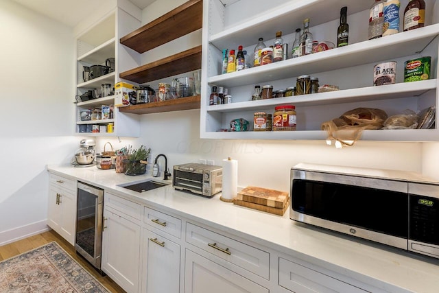 interior space featuring white cabinetry, beverage cooler, sink, and light hardwood / wood-style flooring