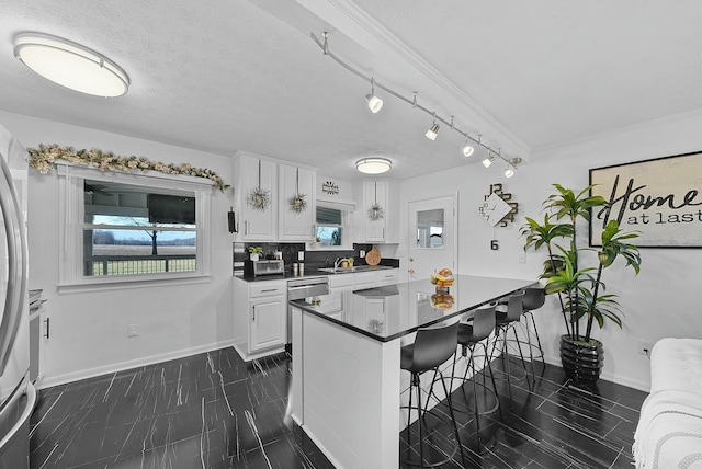 kitchen featuring kitchen peninsula, backsplash, a breakfast bar area, white cabinetry, and sink