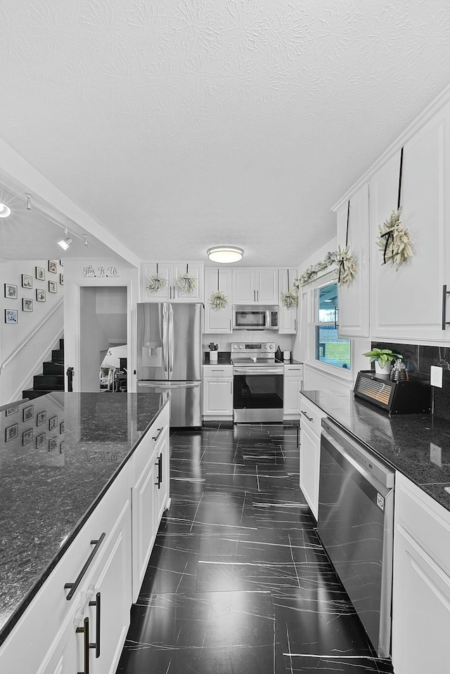 kitchen featuring a textured ceiling, track lighting, white cabinets, appliances with stainless steel finishes, and dark stone countertops