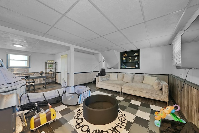 living room with a paneled ceiling, wood walls, and built in shelves