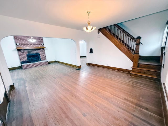 unfurnished living room with wood-type flooring and a brick fireplace