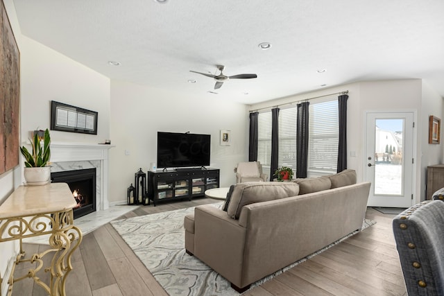 living room featuring a fireplace, ceiling fan, plenty of natural light, and light hardwood / wood-style flooring