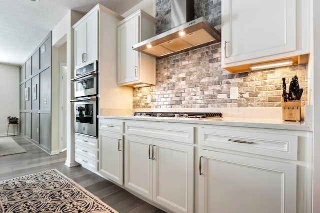 kitchen with hardwood / wood-style floors, stainless steel appliances, a textured ceiling, white cabinetry, and wall chimney range hood