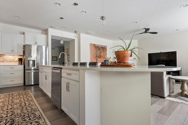 kitchen featuring decorative light fixtures, stainless steel appliances, a kitchen island with sink, and white cabinetry