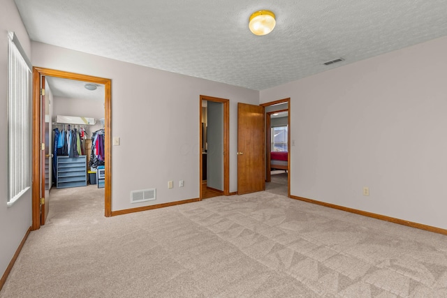 unfurnished bedroom featuring light colored carpet, a closet, a textured ceiling, and a spacious closet