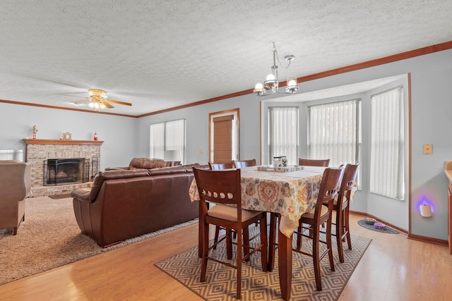 dining room featuring a fireplace, a textured ceiling, light wood-type flooring, ornamental molding, and ceiling fan with notable chandelier