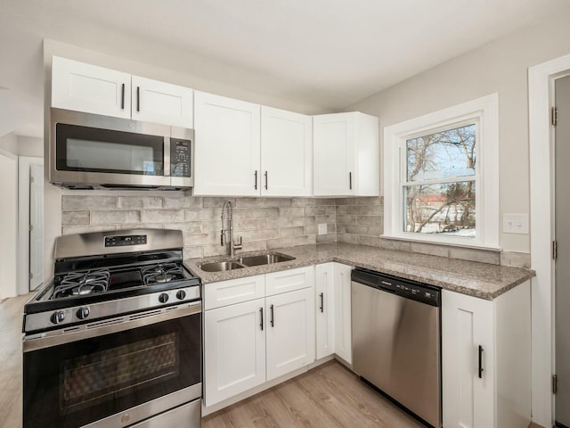 kitchen with light stone counters, stainless steel appliances, white cabinetry, and sink