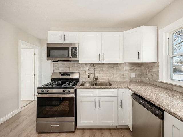 kitchen with stainless steel appliances, light wood-type flooring, light stone counters, sink, and white cabinetry